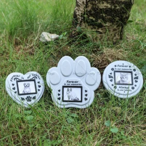 Les trois formes de plaque commémorative — cœur, patte et ronde — posées dans l’herbe, chacune avec son cadre photo