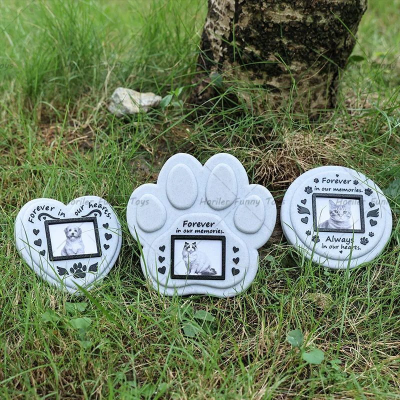 Les trois formes de plaque commémorative — cœur, patte et ronde — posées dans l’herbe, chacune avec son cadre photo